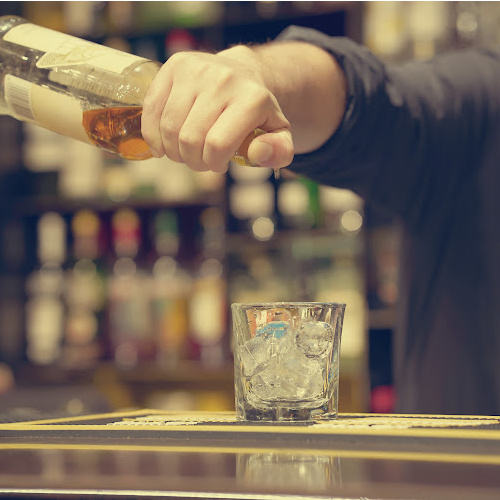 A bartender pouring whiskey over ice at a back bar